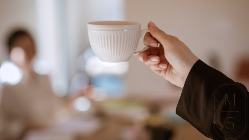 filiżanka kawy trzymana w kobiecej dłoni, widoczny jedwabny rękaw brązowej koszuli